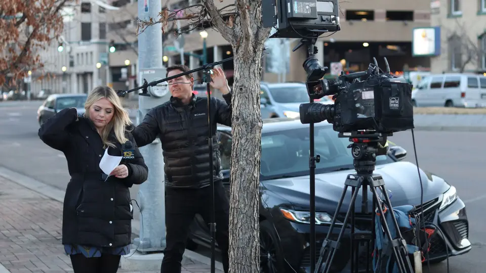 Smartphone with vertical video rig capturing breaking news surrounded by traditional news vans