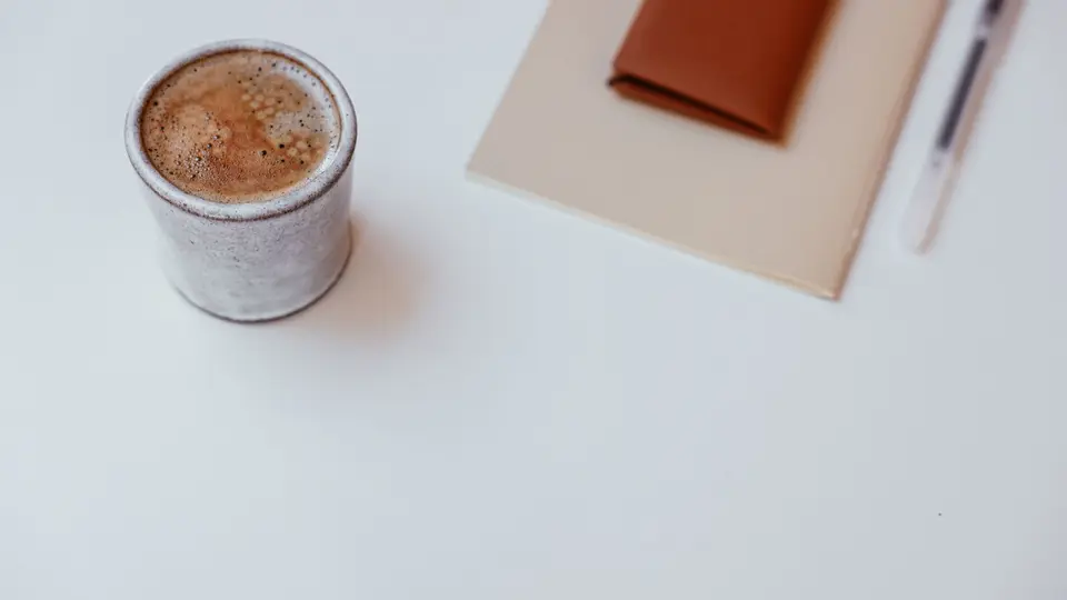 Minimalist ceramic mug, linen notebook, and brass pen on textured concrete desk